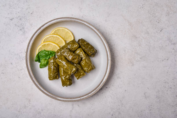 istock Dolma, stuffed grape leaves with rice, meat, sour cream and lemon on light plate 1345690380