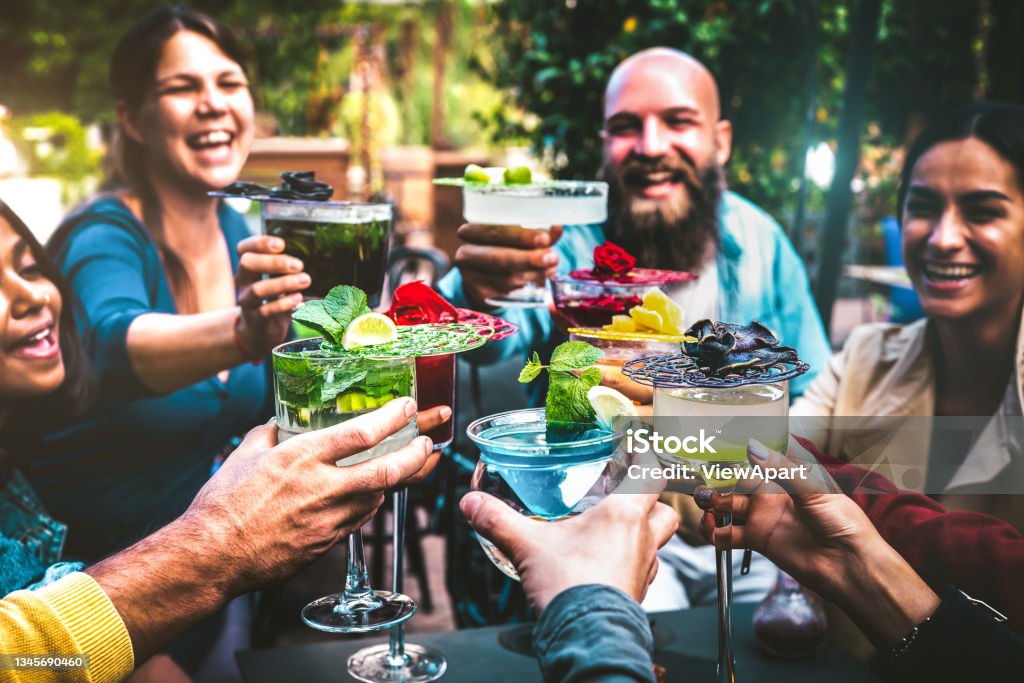 Fashionable people holding multicolored drinks - Trendy friends having fun together drinking cocktails at happy hour - Social gathering party time concept on vintage filter and shallow depth of field Cocktail Party Stock Photo