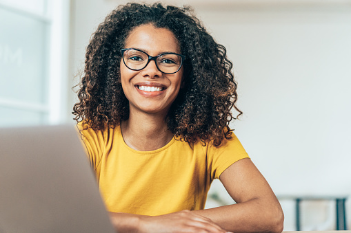 Beautiful smiling mixed race businesswoman dressed casual sitting in office and using laptop.