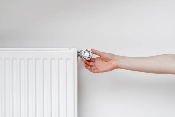 istock Woman adjusting thermostat on white heating radiator 1345696926