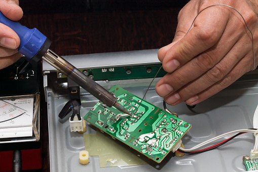 Mans hands soldering power supply electronic circuit  of DVD player with electric soldering iron and tin