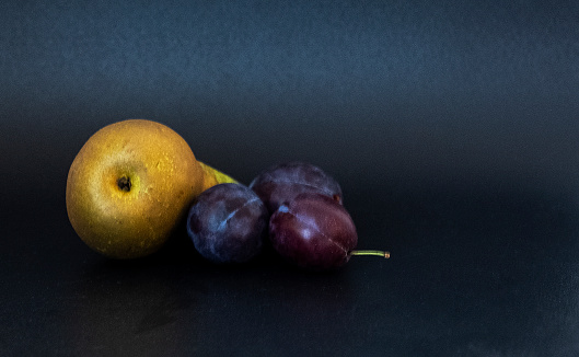 Ripe fruits, pear and plum against a black background. Copy space.