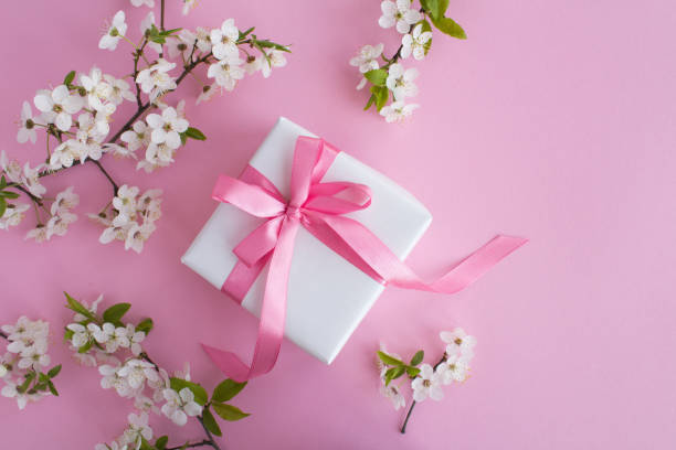 istock Gift with tied pink bow and flowering tree  branches on the pink background. Top view. Copy space. 1345704832