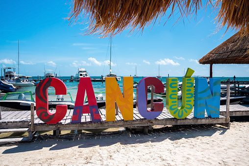 Cancun, Mexico. May 30, 2021. Cancun name sign on wooden pier leading from sand into sea with moored yachts or sailboat on water surface