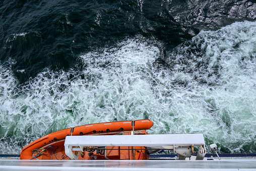 Lifeboat hanging on the ship side with frothy water underneath.