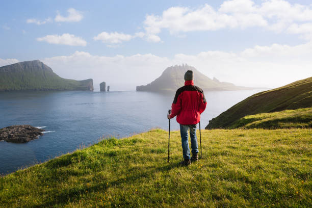 The view of the Drangarnir sea stacks and the Tindholmur islet, Faroe Islands The view of the Drangarnir sea stacks and the Tindholmur islet, Faroe Islands. A tourist in a red jacket enjoying the beautiful nature vágar photos stock pictures, royalty-free photos & images
