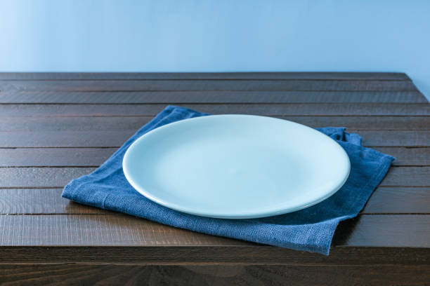 istock Empty plate on napkin on wooden table over grunge blue background. 1345715529