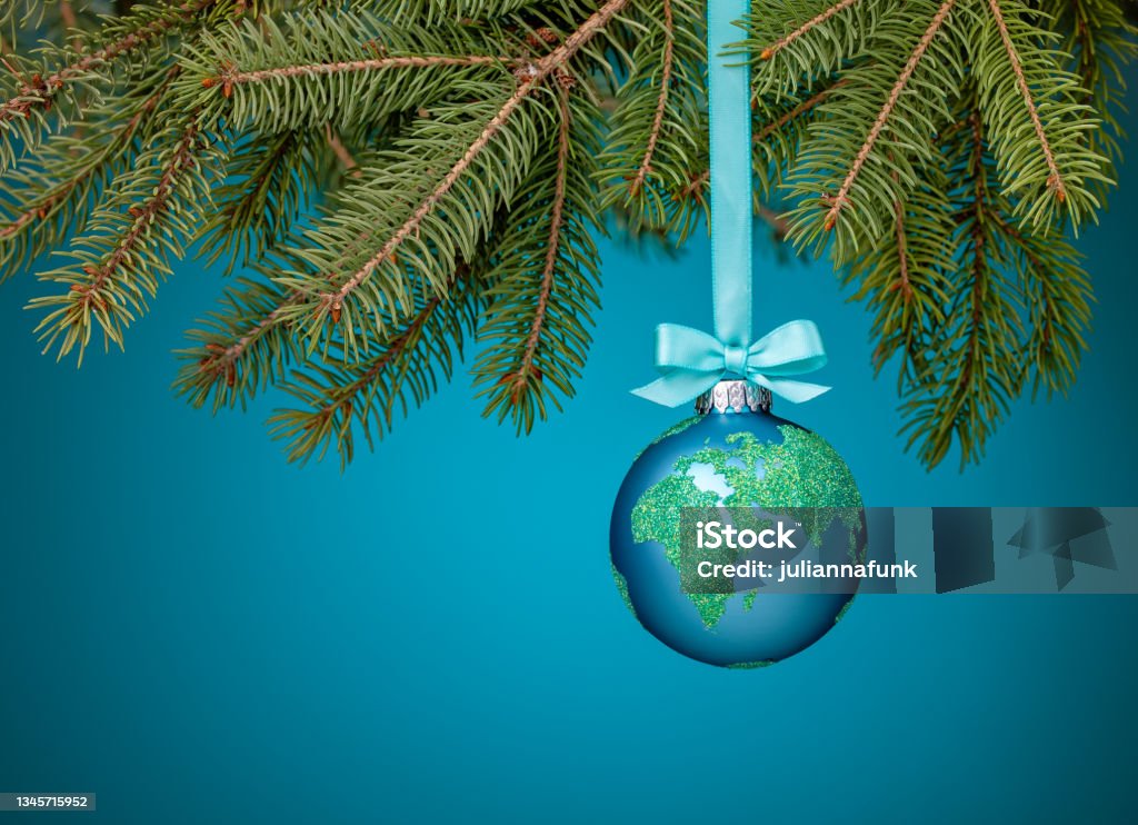 Globe Christmas Ornament hanging Globe Christmas ornament with bow hanging from a tree branch on blue. Peace on Earth, eco friendly or winter travel concept. Christmas Stock Photo