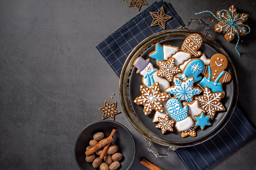 Decorated Blue and White iced gingerbread Christmas cookies on rustic platter with spices. Dark Grey background. Top view with copyspace