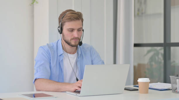 istock Creative Man Wearing Headset Working on Laptop in Office 1345717449