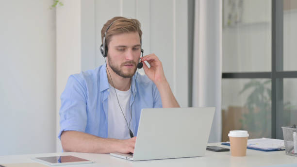 istock Creative Man Talking on Headset, Working on Laptop in Office 1345717776