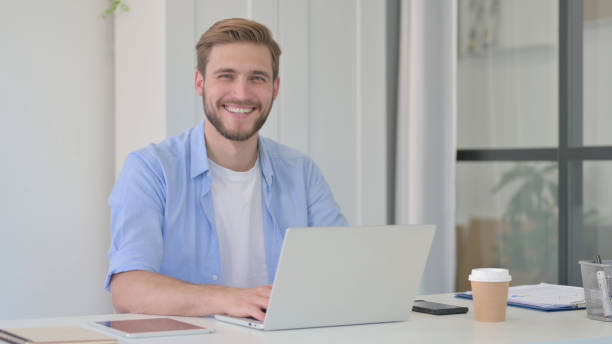 istock Young Creative Man with Laptop Smiling at Camera 1345718682