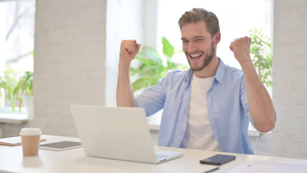 istock Successful Young Creative Man Celebrating on Laptop in Modern Office 1345719532