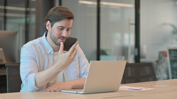 istock Angry Casual Young Man with Laptop Talking on Phone 1345721217