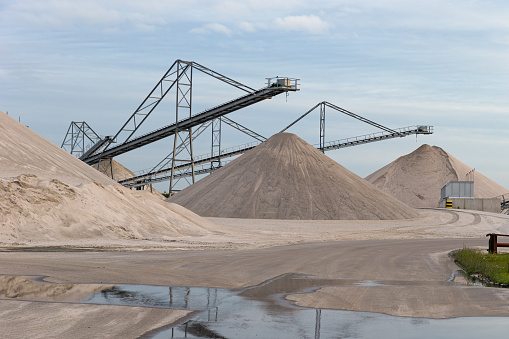 Quarry with heaps of sand and conveyer belts, reflecting in water