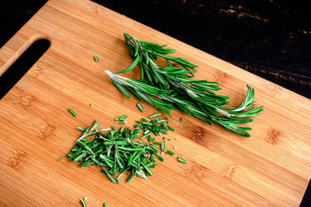 Minced rosemary leaves on a wooden cutting board