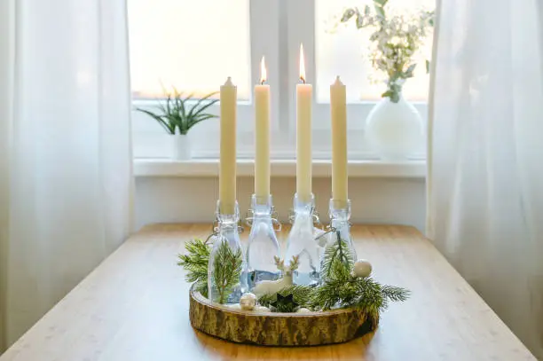 alternative advent wreath, candles in bottles on a wooden board with decoration on a table at the window, two are lit, second sunday before christmas, copy space, selected focus, narrow depth of field