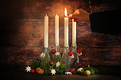 First advent, hand lighting one of four candles placed in bottles with fir branches and christmas decoration against a rustic dark wooden background, copy space