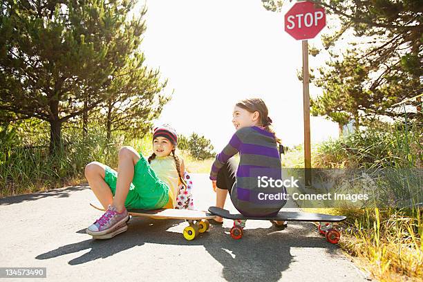 Girls Sitting On Skateboards Along Rural Road Stock Photo - Download Image Now - Portland - Oregon, Summer, 8-9 Years