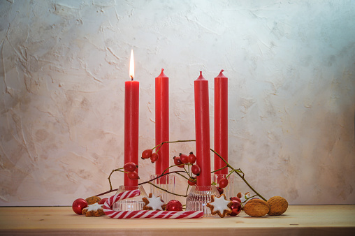 Four red candles, one is lit for the first Sunday before Christmas, Advent decoration on a wooden table against a rustic wall, copy space, selected focus, narrow depth of field