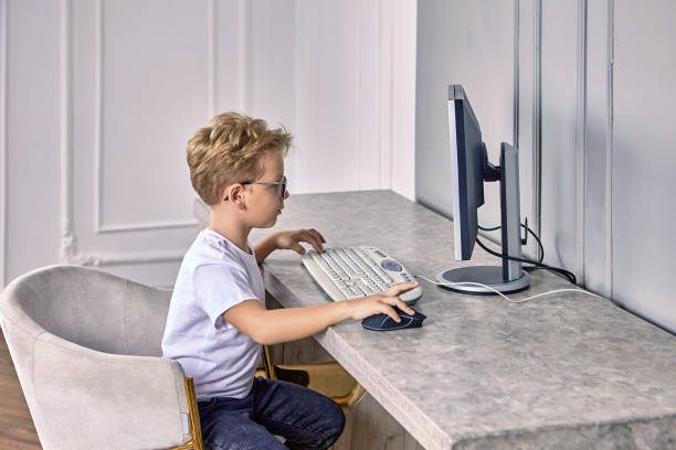 el niño de 6 años con gafas se sienta detrás de la computadora en casa. - eyewear child glasses 6 7 years fotografías e imágenes de stock