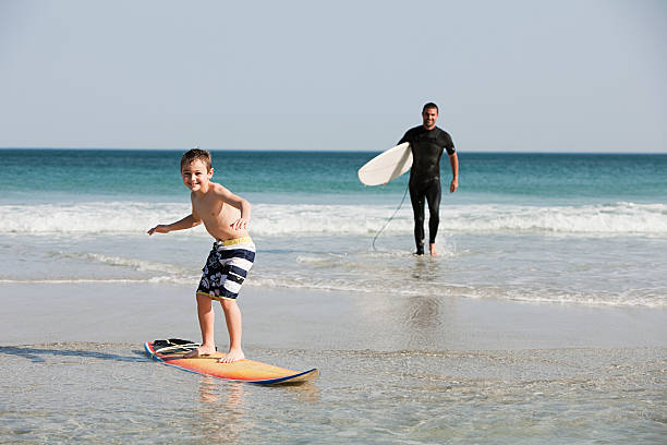 młody chłopiec surfing w płytkiej wodzie, - surfing role model learning child zdjęcia i obrazy z banku zdjęć