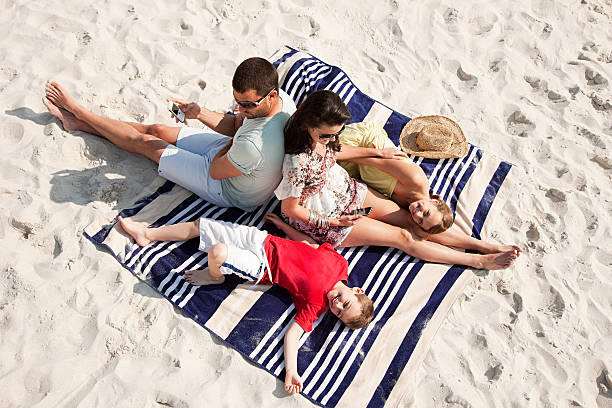 familie sitzen zusammen und liegen auf einem teppich am strand - strandhandtuch stock-fotos und bilder