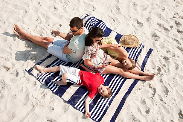 família sentada e deitado juntos em um tapete em uma praia - summer beach vacations sand - fotografias e filmes do acervo