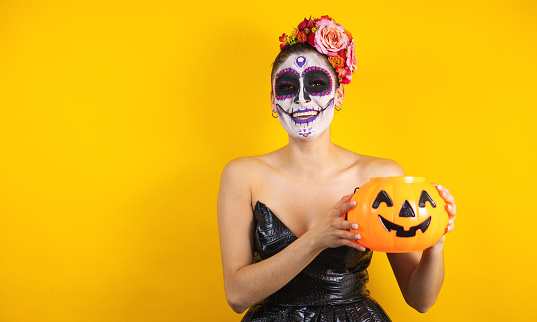 Mexican Catrina, portrait of young latin woman holding a plastic calaverita pumpkin for Halloween party in Mexico