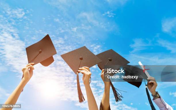 Four Hands Holding Graduation Hats On Background Of Blue Sky Stock Photo - Download Image Now