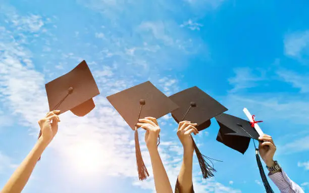 Photo of Four hands holding graduation hats on background of blue sky