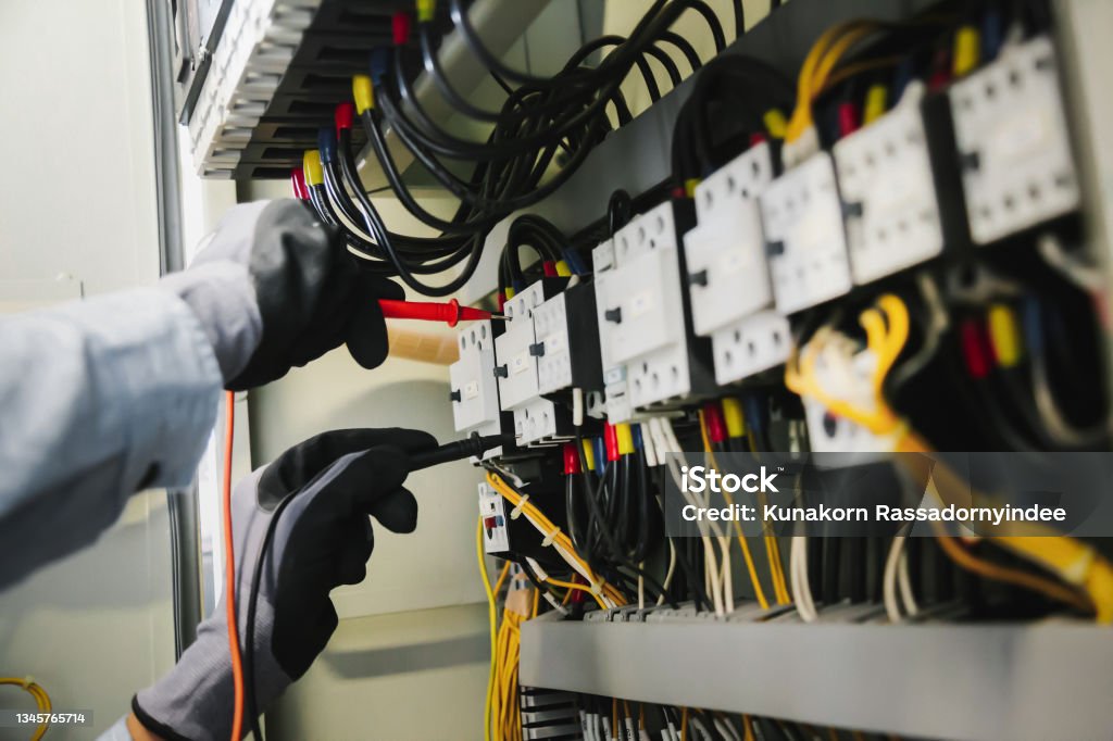Electrical engineers test electrical installations and wiring on protective relays, measuring them with a multimeter. Electricity Stock Photo