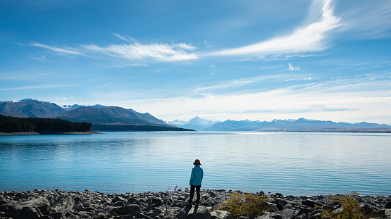 Woman standing on the shore of Lake Pukaki, enjoying the views of Mt Cook and Southern Alps, South Island.