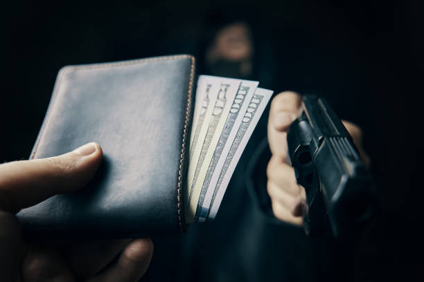 Man's hand holds out purse of money to robber with gun. Armed robbery. Man's hand holds out wallet of money to robber with gun. Hundred and fifty dollars in open purse. Firearm is pointed at camera. Criminal in hood and mask. Assault on unarmed man. wallet gun stock pictures, royalty-free photos & images