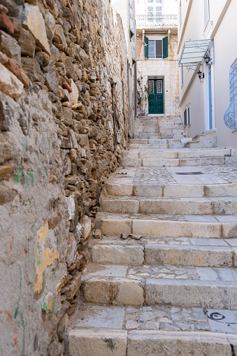 Paved empty narrow exterior stairs bellow to upper way next to aged stonewall at Syros island, Cyclades destination Greece. Stairway drives to traditional house at Ermoupoli city summer day. Vertical