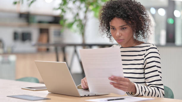 istock Focused African Woman with Laptop Reading Documents in Office 1345783504