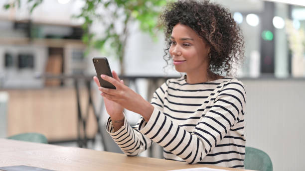 istock Serious African Woman Browsing Internet on Smartphone in Office 1345784371