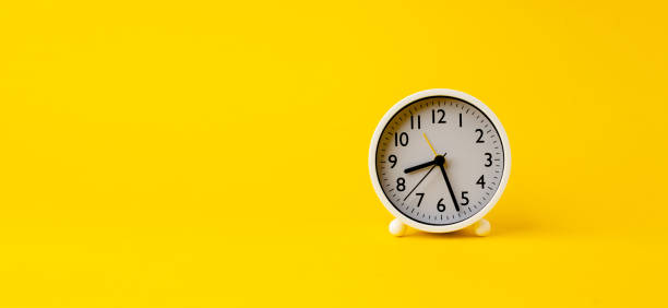 white alarm clock on yellow background with space for text, time ideas and work