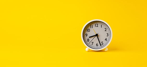 white alarm clock on yellow background with space for text, time ideas and work