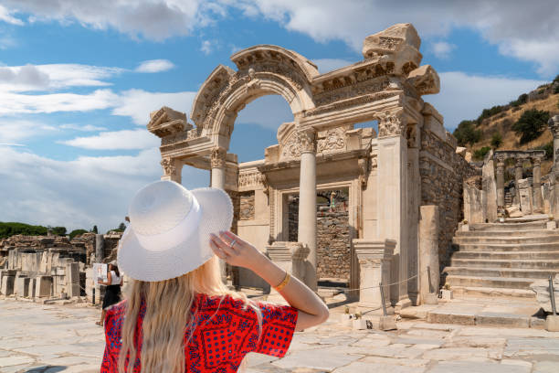 vista trasera de una chica con vestido rojo y sombrero blanco observa las ruinas del templo de adriano en la antigua ciudad de éfeso, turquía, en un soleado día de verano, efes, izmir, turquía - ephesus fotografías e imágenes de stock