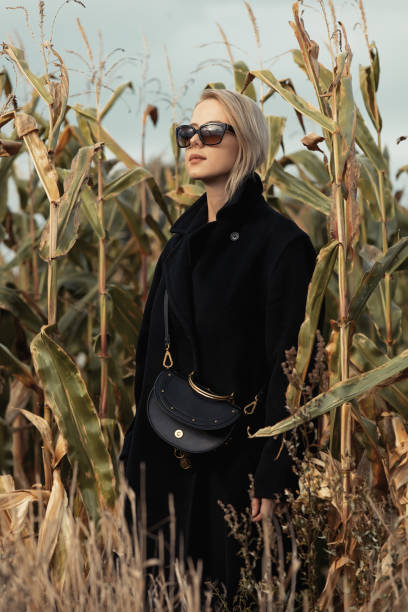 stylowa kobieta w czarnym płaszczu na jesiennym polu kukurydzy - autumn clothing corn crop fashion zdjęcia i obrazy z banku zdjęć
