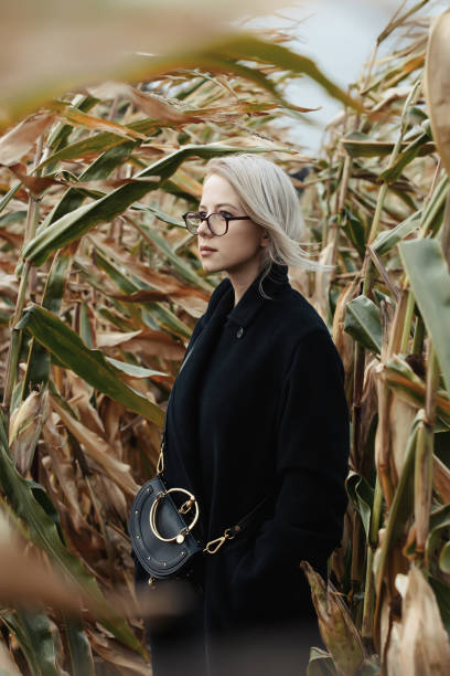 stylowa kobieta w czarnym płaszczu na jesiennym polu kukurydzy - autumn clothing corn crop fashion zdjęcia i obrazy z banku zdjęć