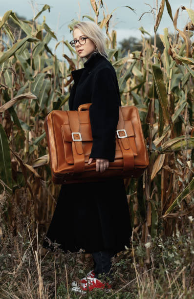 stylowa kobieta w czarnym płaszczu z walizką na jesiennym polu kukurydzy - autumn clothing corn crop fashion zdjęcia i obrazy z banku zdjęć