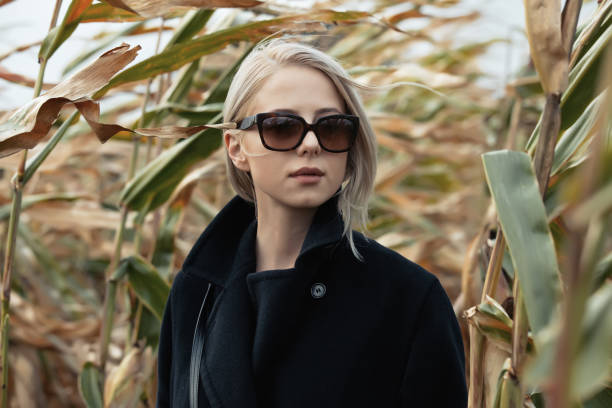 stylowa kobieta w czarnym płaszczu i szklankach na jesiennym polu kukurydzy - autumn clothing corn crop fashion zdjęcia i obrazy z banku zdjęć