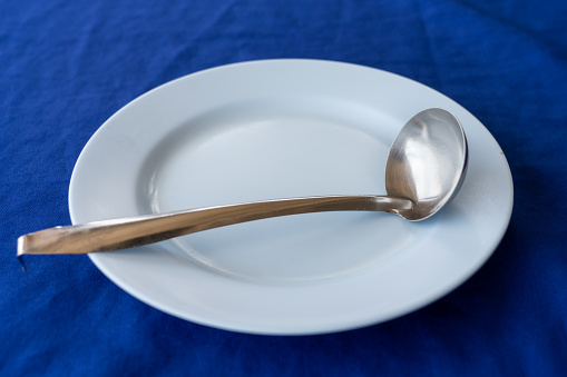 Stainless steel ladle on a white plastic plate