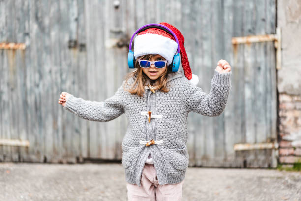 menina engraçada usando chapéu de papai noel e óculos de sol dançando contra um fundo grunge de madeira ao ar livre na época de natal - feliz natal & ano novo - conceito de infância nos dias de natal - child dancing preschooler outdoors - fotografias e filmes do acervo