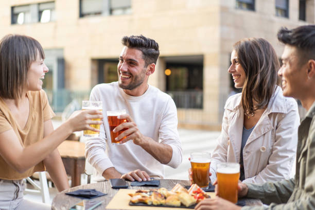 glückliche freunde trinken bier in der außenkneipe in der stadt - freundschafts-lifestyle-konzept mit jungen millennials, die die gemeinsame zeit in der open-air-kneipe genießen - freunde imbiss großstadt stock-fotos und bilder