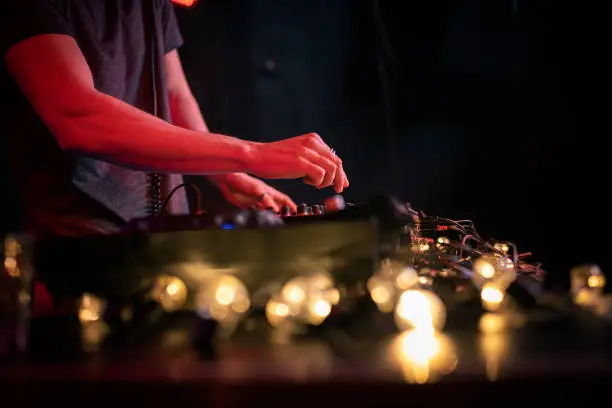 View of an unrecognizable club DJ, mixing the song on turntable in the night club