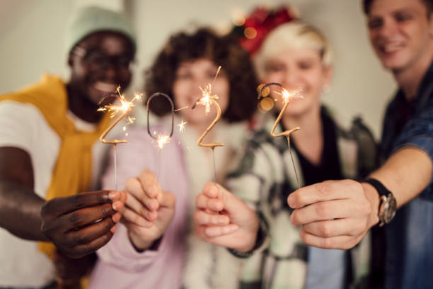 Group of teenagers lighting sprinklers and celebrating New Year Portrait of a multi - ethnic group of young people lighting sprinklers and celebrating the New Year's eve at home. 21 24 months stock pictures, royalty-free photos & images