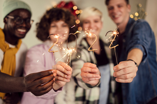 Portrait of a multi - ethnic group of young people lighting sprinklers and celebrating the New Year's eve at home.